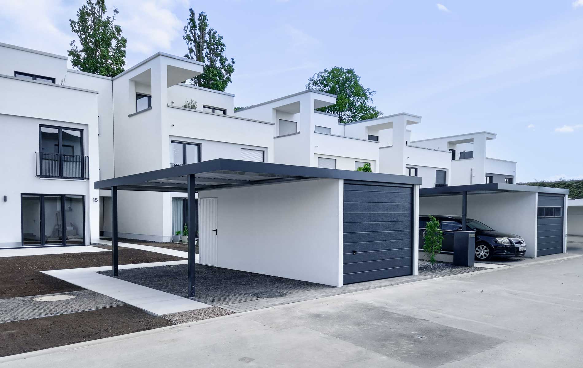 Anbaucarports an Stahlgarage von Siebau. Beide Garagen mit Sektionaltor. Rechte Garage mit Fensterband im Sektionaltor