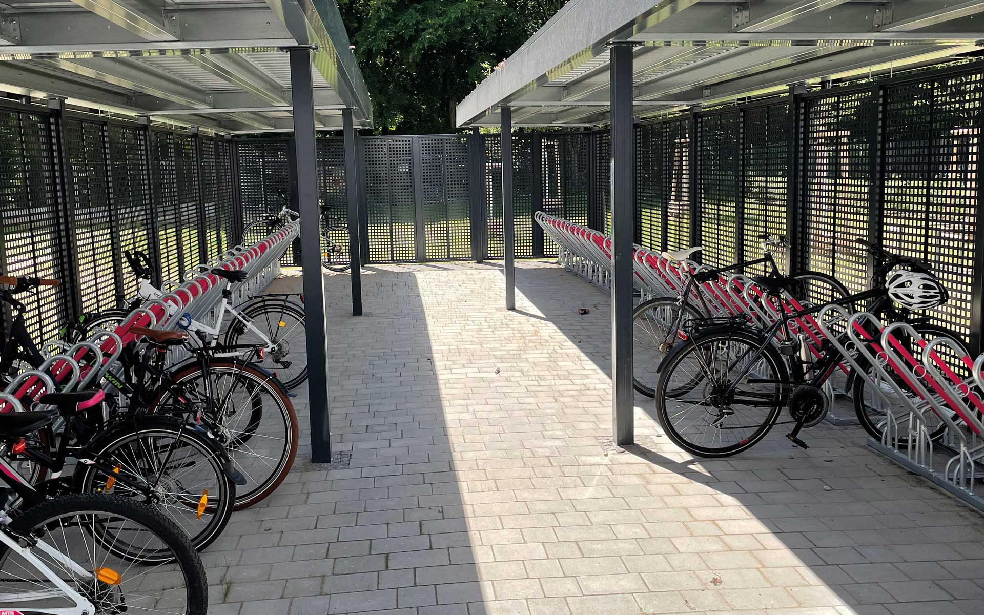 Fahrradüberdachung mit Teilverkleidung der Rück- und Seitenwand. Sichtschutzelemente mit Quadratlochung. Ausstattung der Anlage mit Fahrradparkern inkl. Anlehnbügel